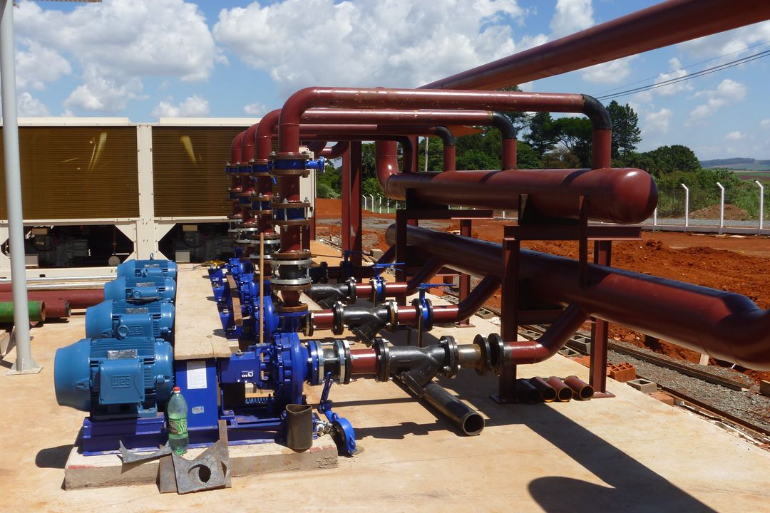 Conjunto de bombas e tubulação industrial instalado sobre base de concreto ao lado de equipamentos de refrigeração.