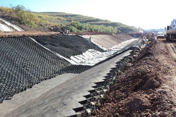 Canal de drenagem revestido com geocélulas e proteção de talude, com equipamentos trabalhando ao longo da vala.