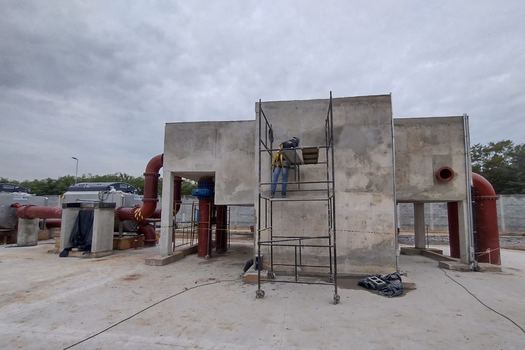 Estruturas de concreto e tubulação de uma instalação industrial de tratamento, com trabalhador em andaime.