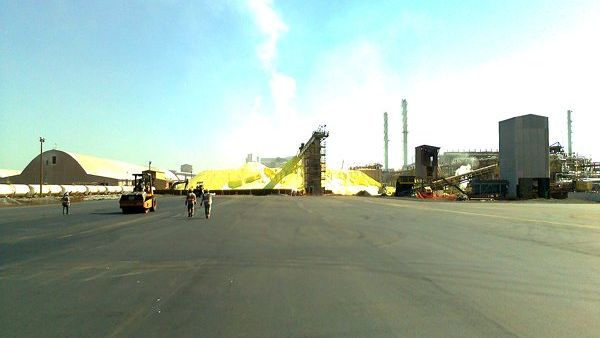 Rolo compactador e equipe concluindo a pavimentação de um pátio extenso junto a uma planta industrial.
